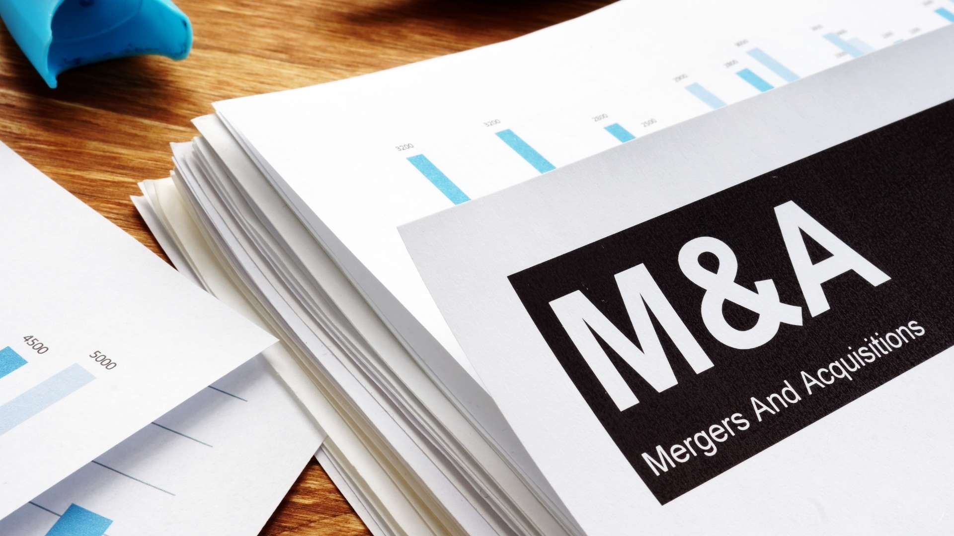 Stack of M&A documents with charts representing merger and acquisition data