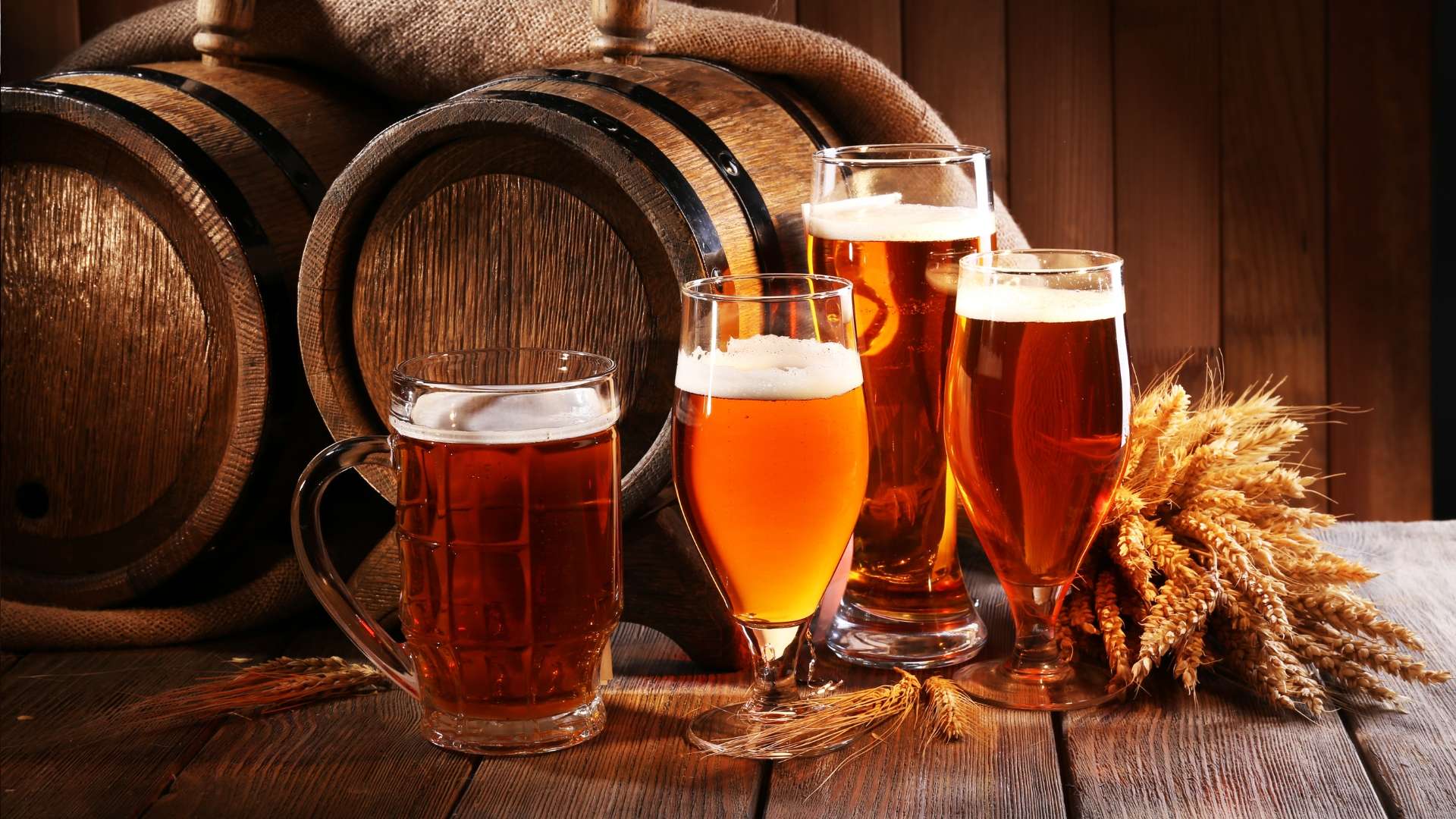 Glasses of craft beer with wooden barrels and wheat on a rustic table