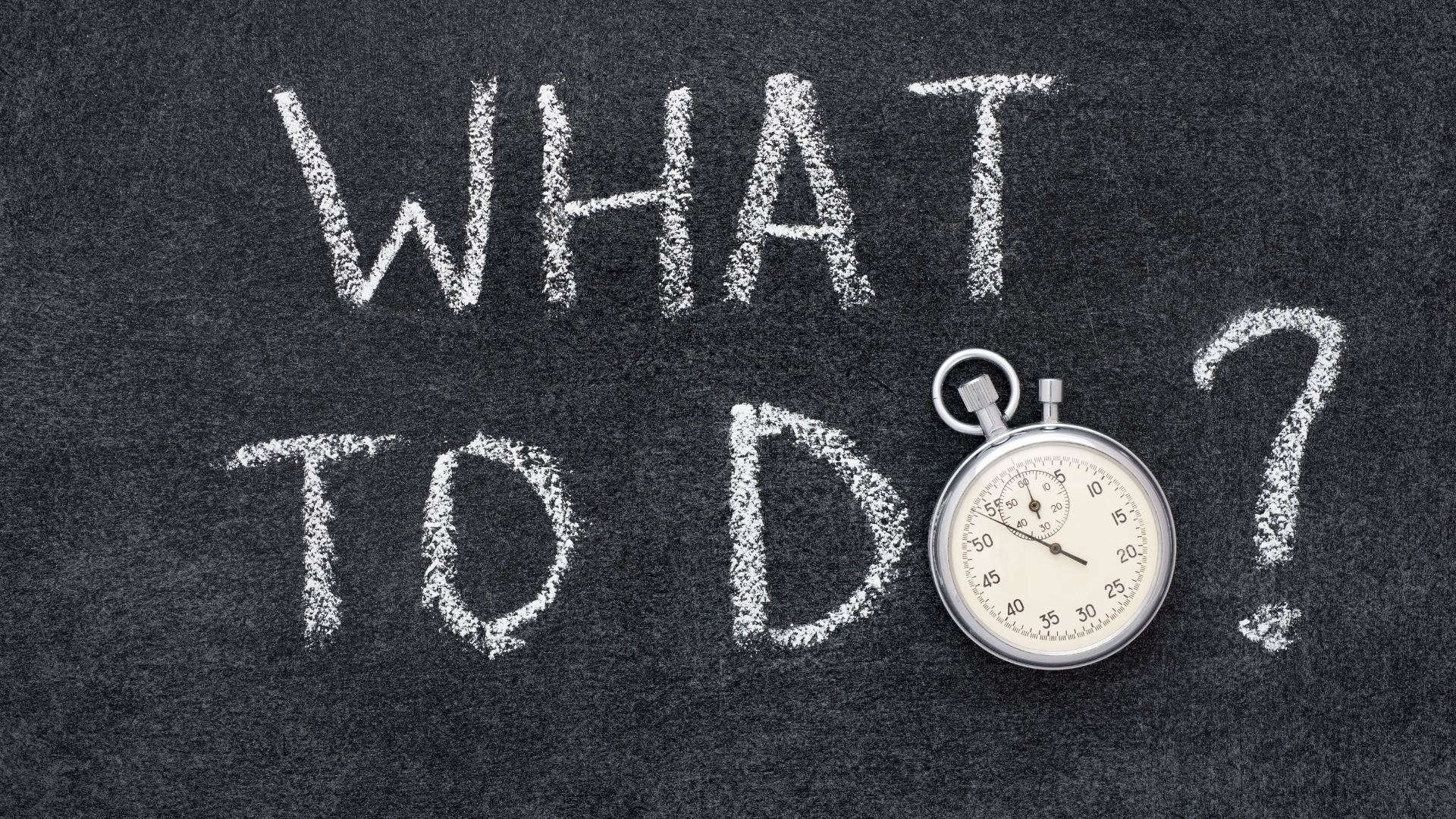 Chalkboard with the words “What to Do?” written in white chalk alongside a stopwatch, symbolizing urgency in taking action.