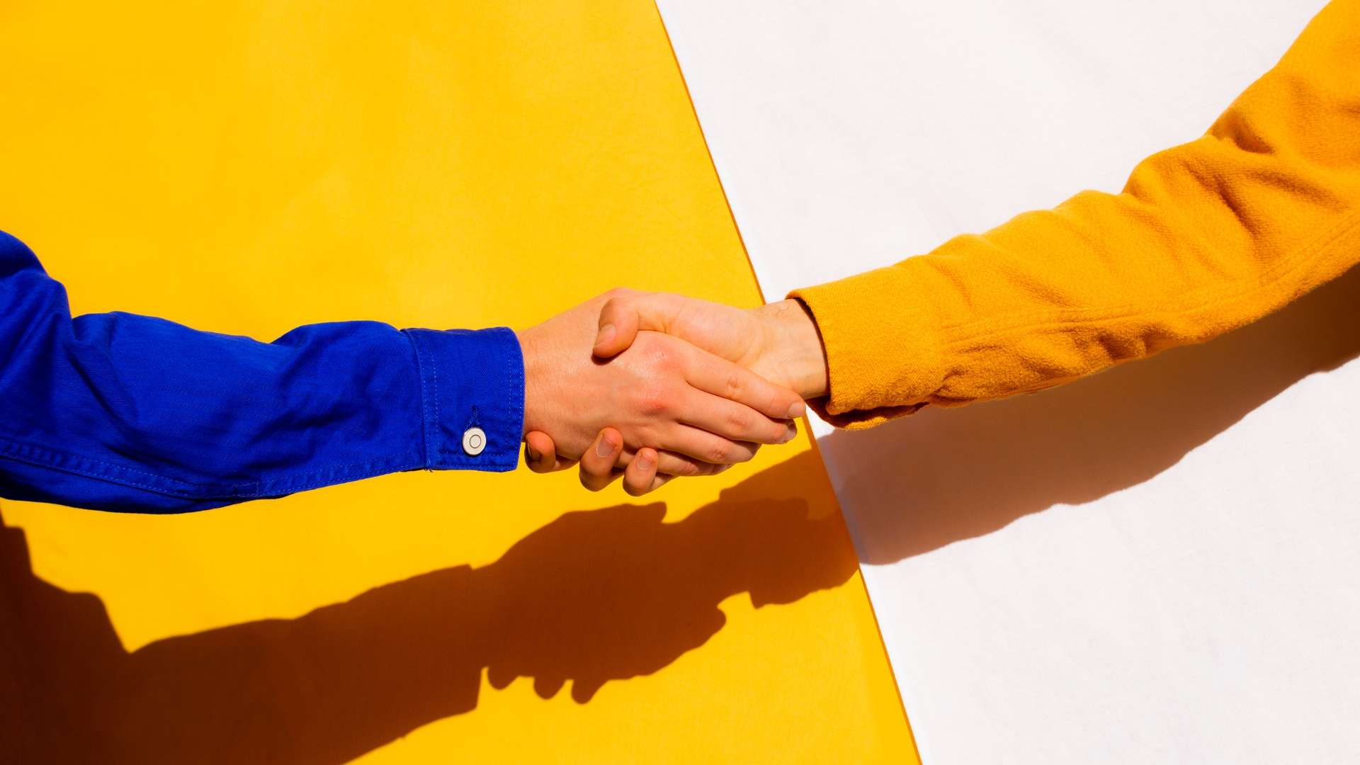 Close-up of two people shaking hands against a yellow and white background, symbolizing a business agreement.