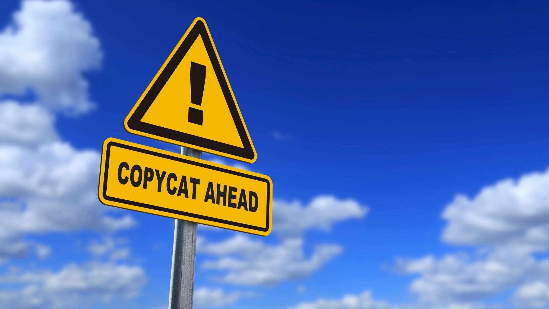 A yellow road sign with an exclamation mark and the words "Copycat Ahead" against a blue sky with clouds.