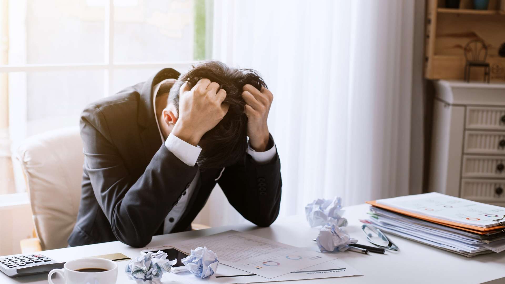 Stressed business professional holding head in frustration over documents and crumpled papers, symbolizing the impact of copyright infringement on marketing strategies.