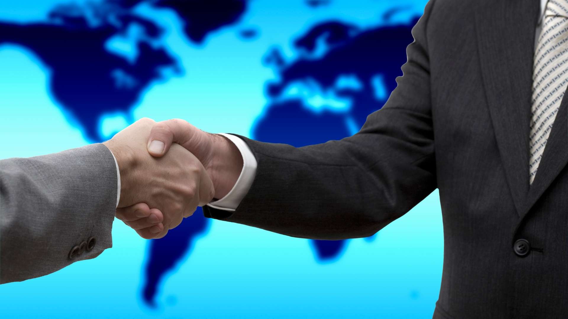 Two business professionals shaking hands in front of a world map, symbolizing international partnerships and global brand protection.