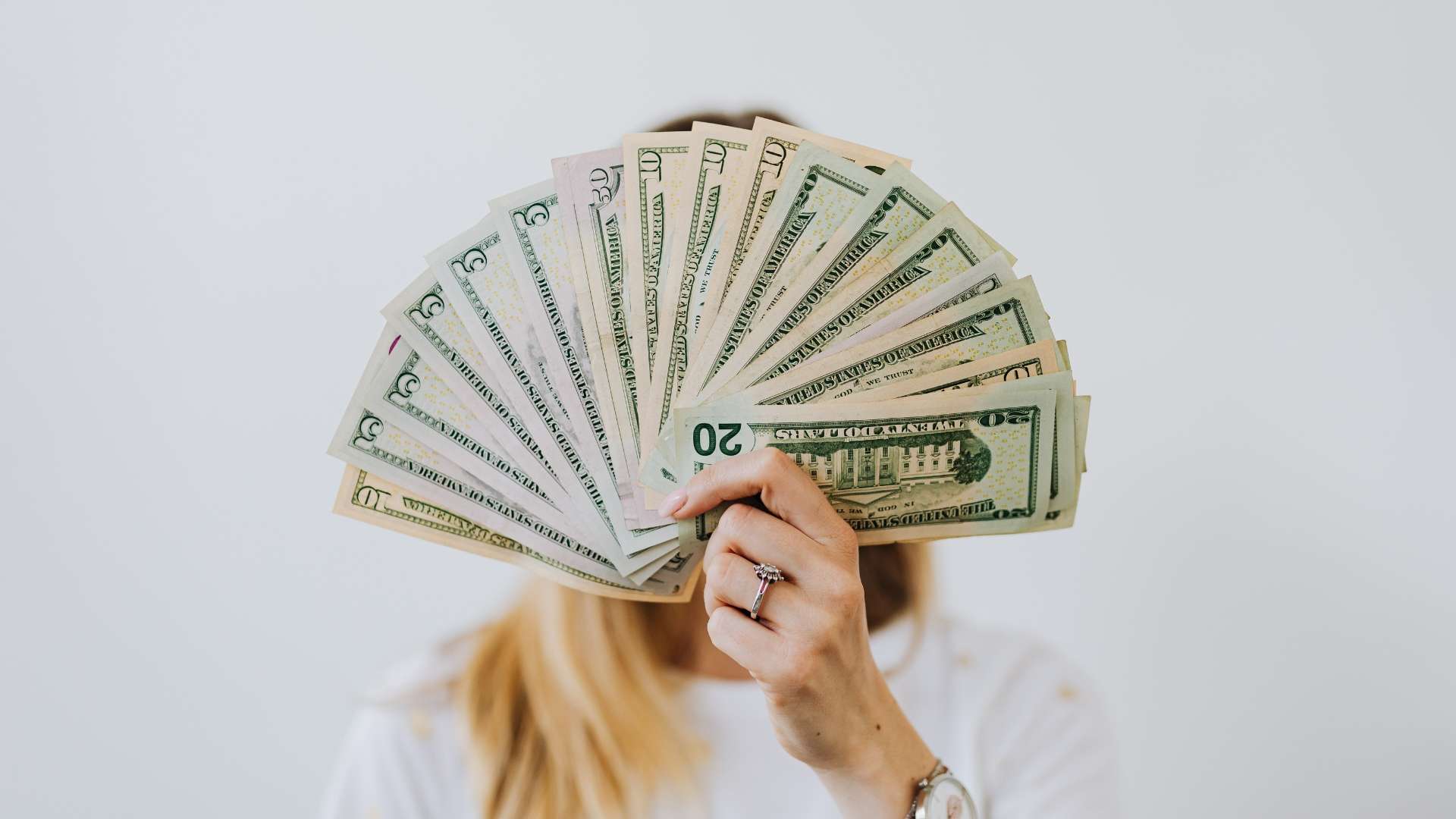 Person holding a fan of U.S. dollar bills, representing financial rewards and equity compensation benefits.