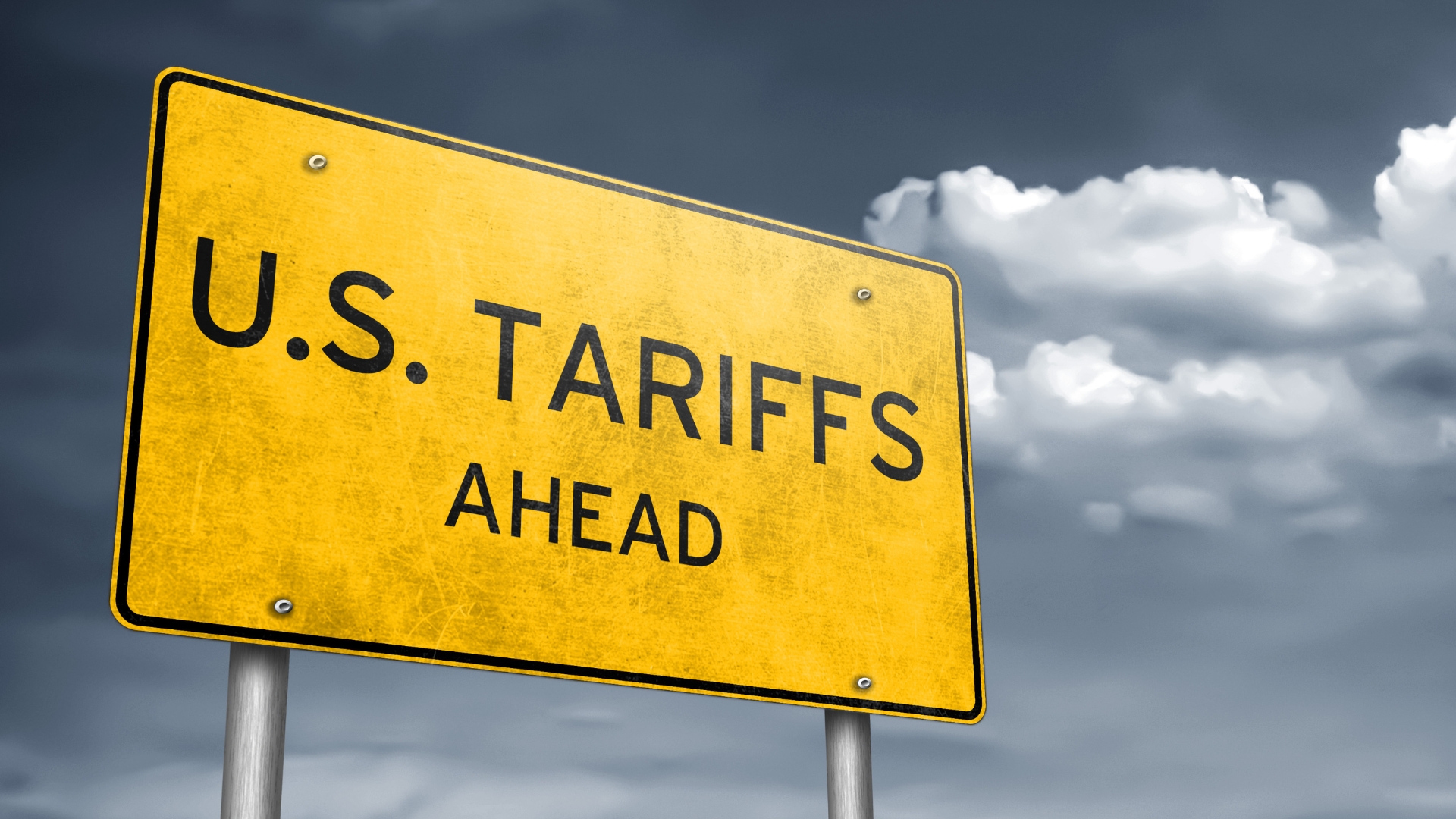 Yellow road sign reading “U.S. Tariffs Ahead” against a cloudy sky, symbolizing rising tariff risks for businesses.