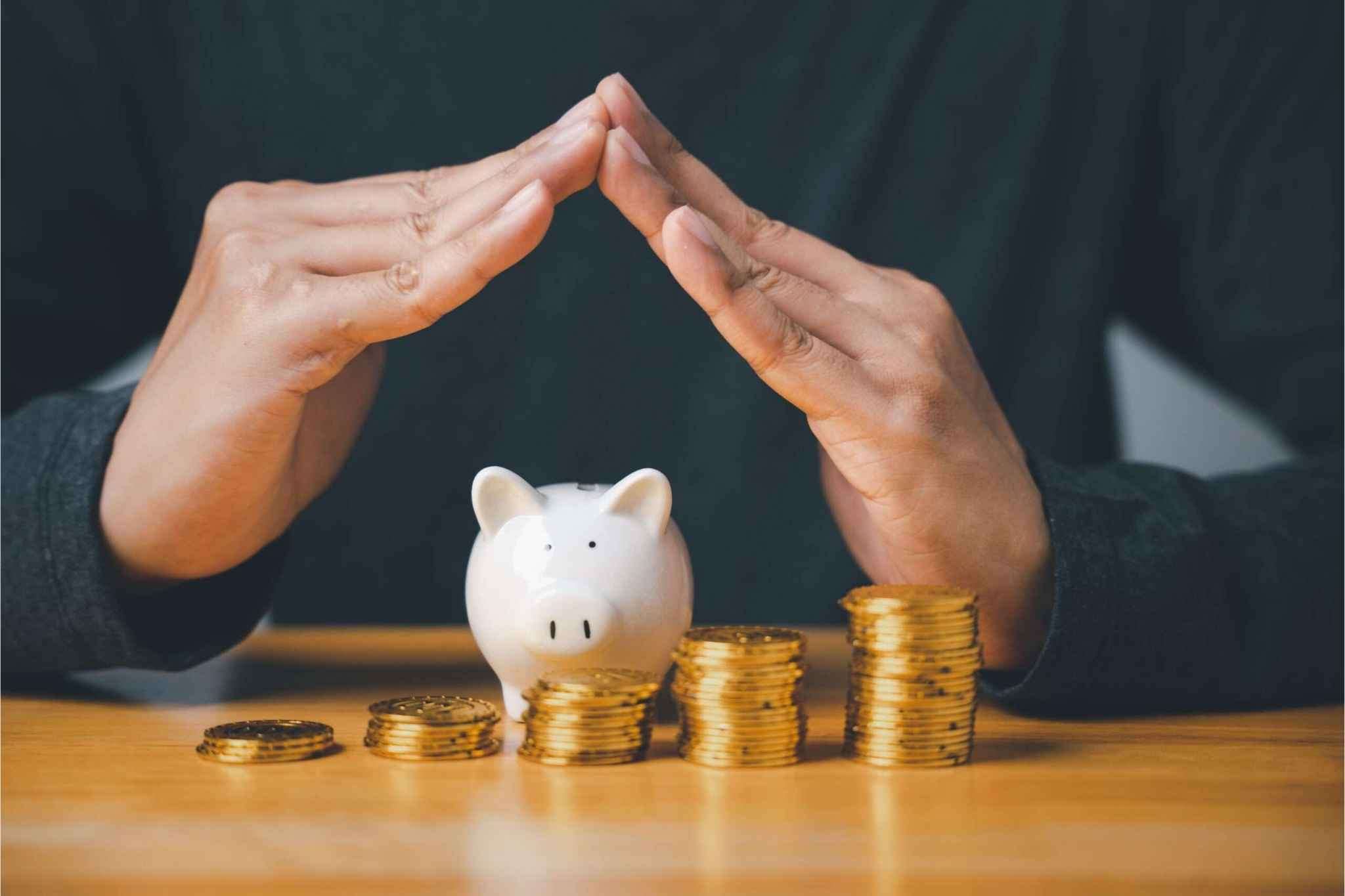 Hands forming a protective shelter over a piggy bank and growing stacks of gold coins, representing the protection of financial equity and fair market valuation.