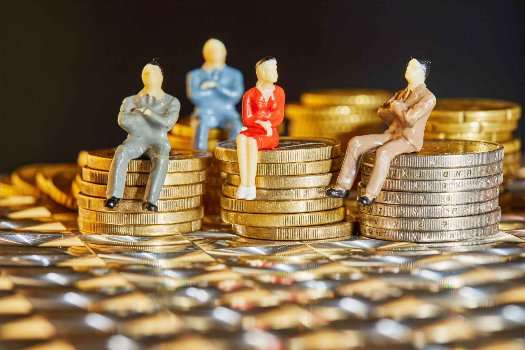 Four miniature professional figurines sitting on stacks of gold coins of varying heights, set against a reflective silver surface. This visual metaphor illustrates equity compensation as a strategic tool to attract and retain top talent.