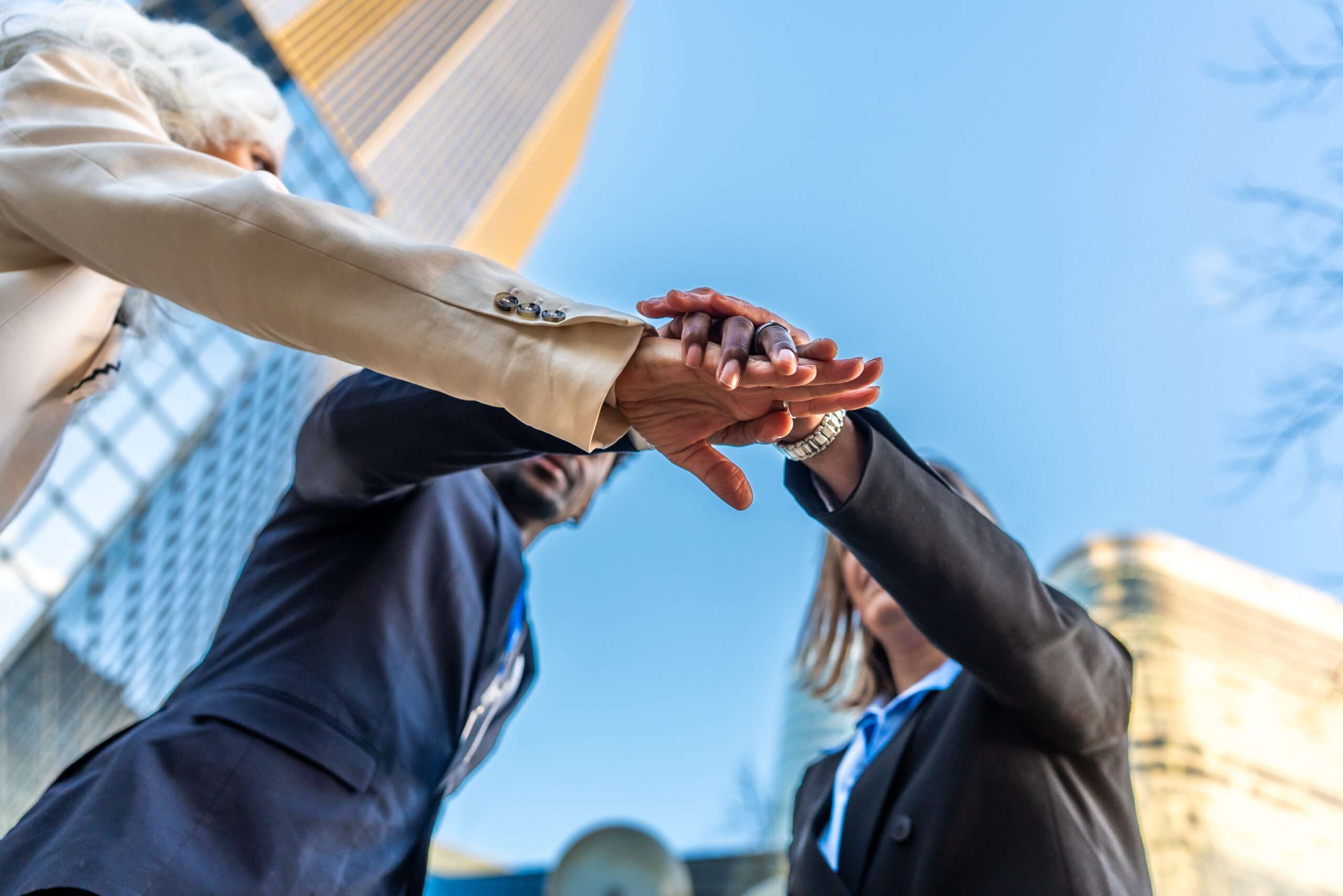 Three diverse business partners stacking hands in unity, symbolizing the initial "honeymoon phase" of a new LLC partnership before conflicts arise.