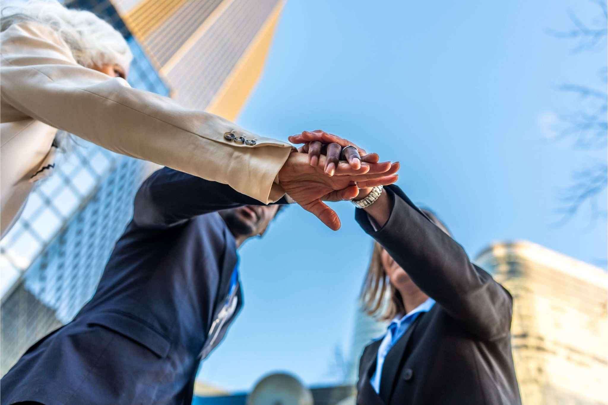 Three diverse business partners stacking hands in unity, symbolizing the initial "honeymoon phase" of a new LLC partnership before conflicts arise.