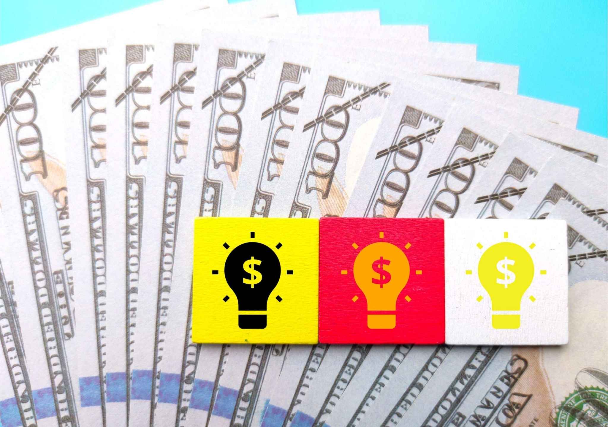 A top view of colorful wooden squares with a drawing of light bulbs on dollar banknotes - business concept