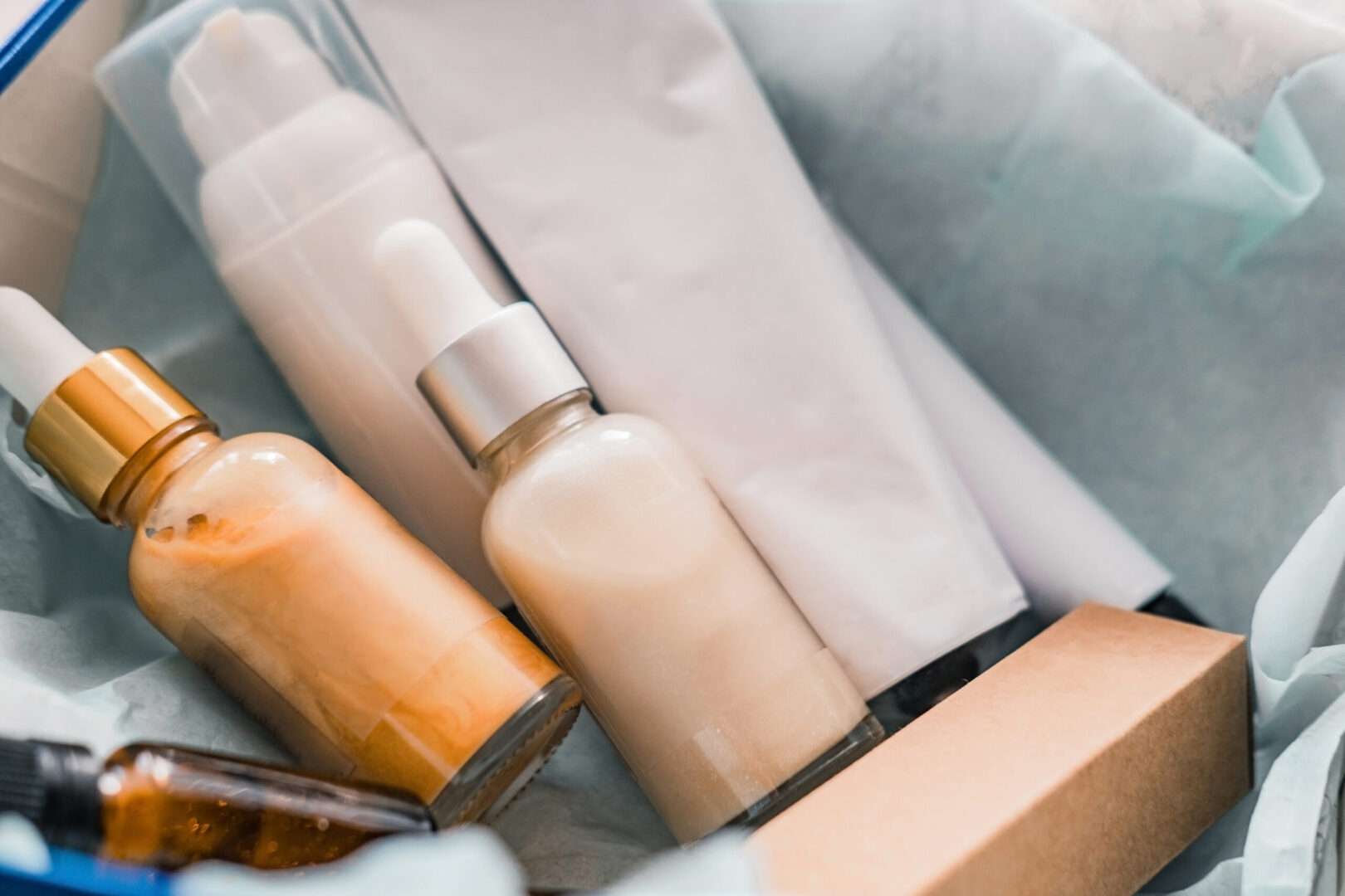 Natural cosmetic skincare products including amber dropper bottles, a pump bottle, and a tube displayed in a gift box with tissue paper, representing product packaging design that requires trademark, copyright, and trade dress protection for small business brands in Los Angeles