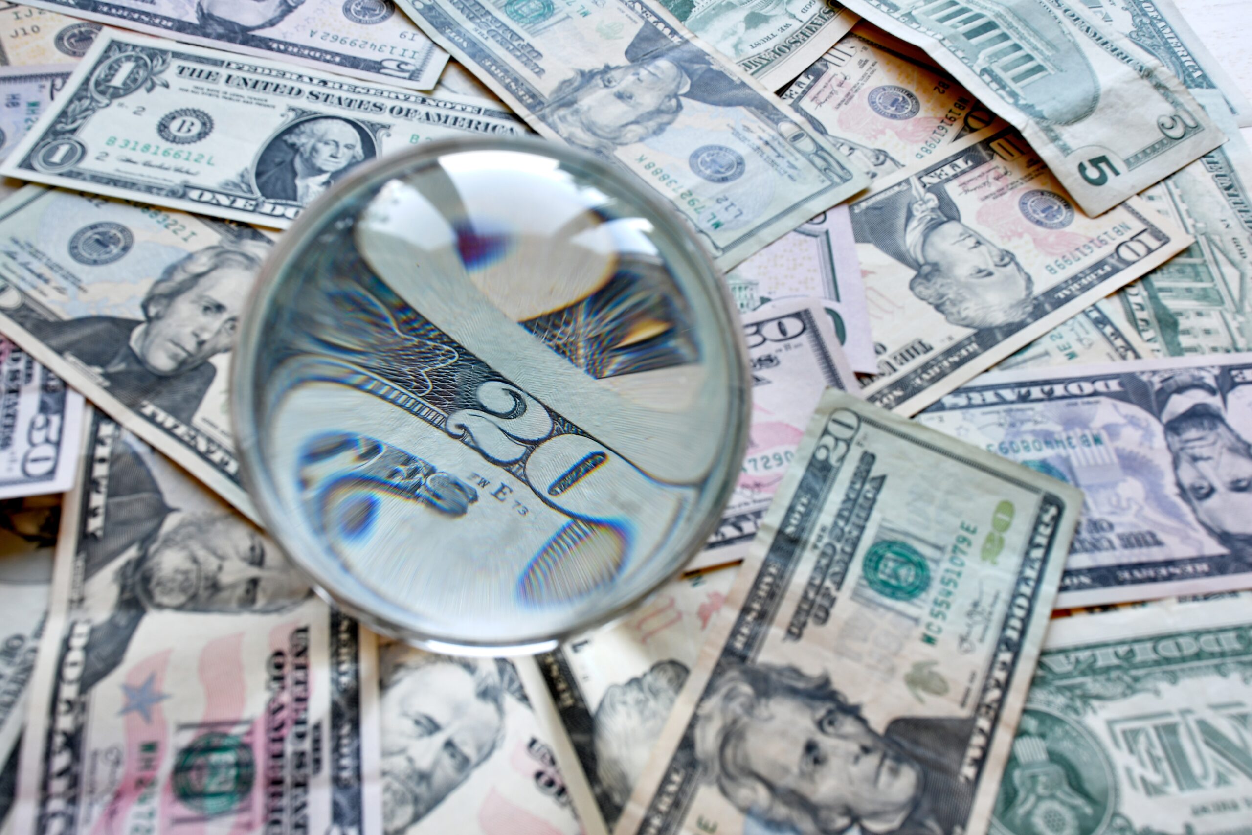 A magnifying glass examining US dollar bills, representing the financial value and careful scrutiny required when securing global trademark protection for DTC brands.