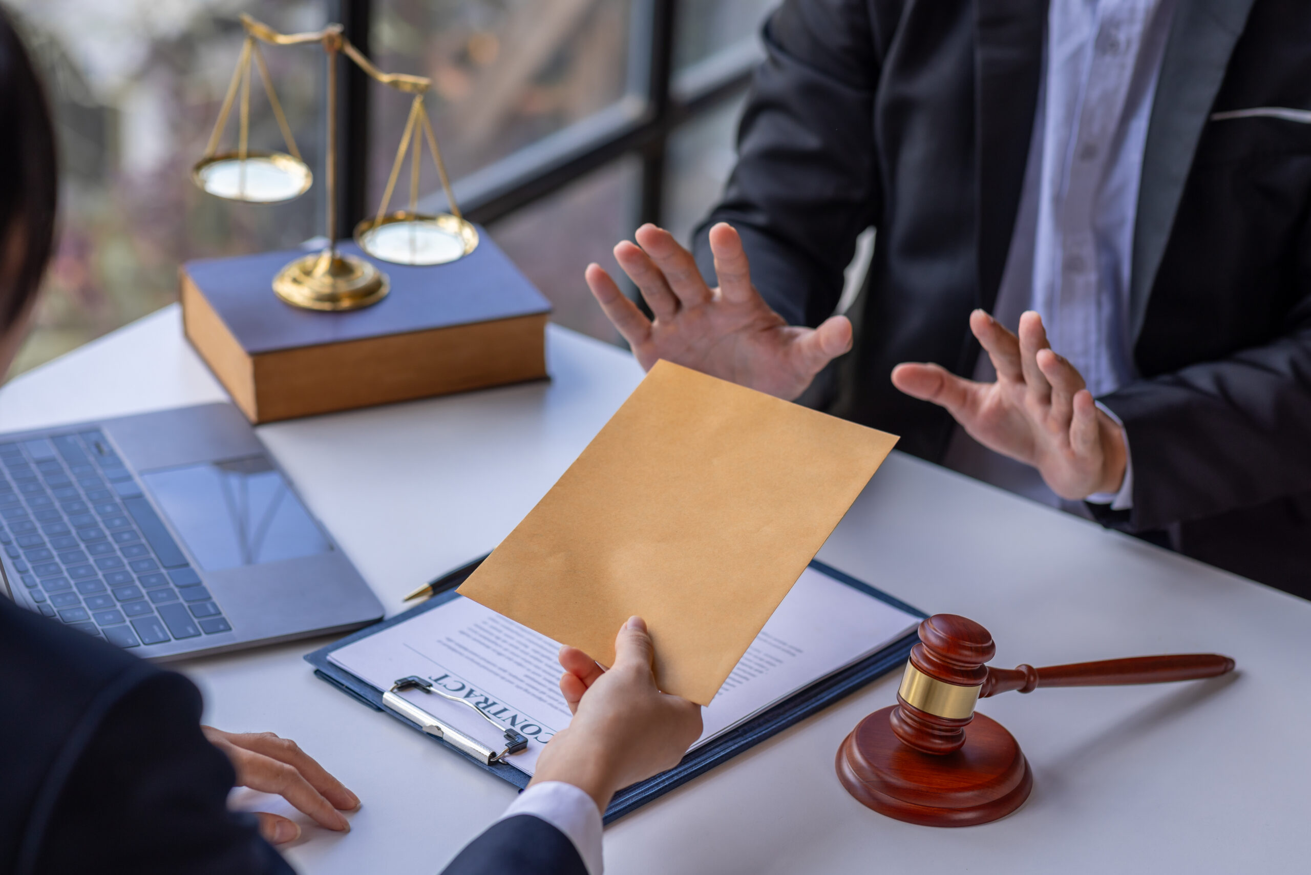 A business professional refusing a document envelope across a legal desk with a gavel, contract, and scales of justice, representing the decision to reject or respond to a cease and desist letter for trademark infringement.