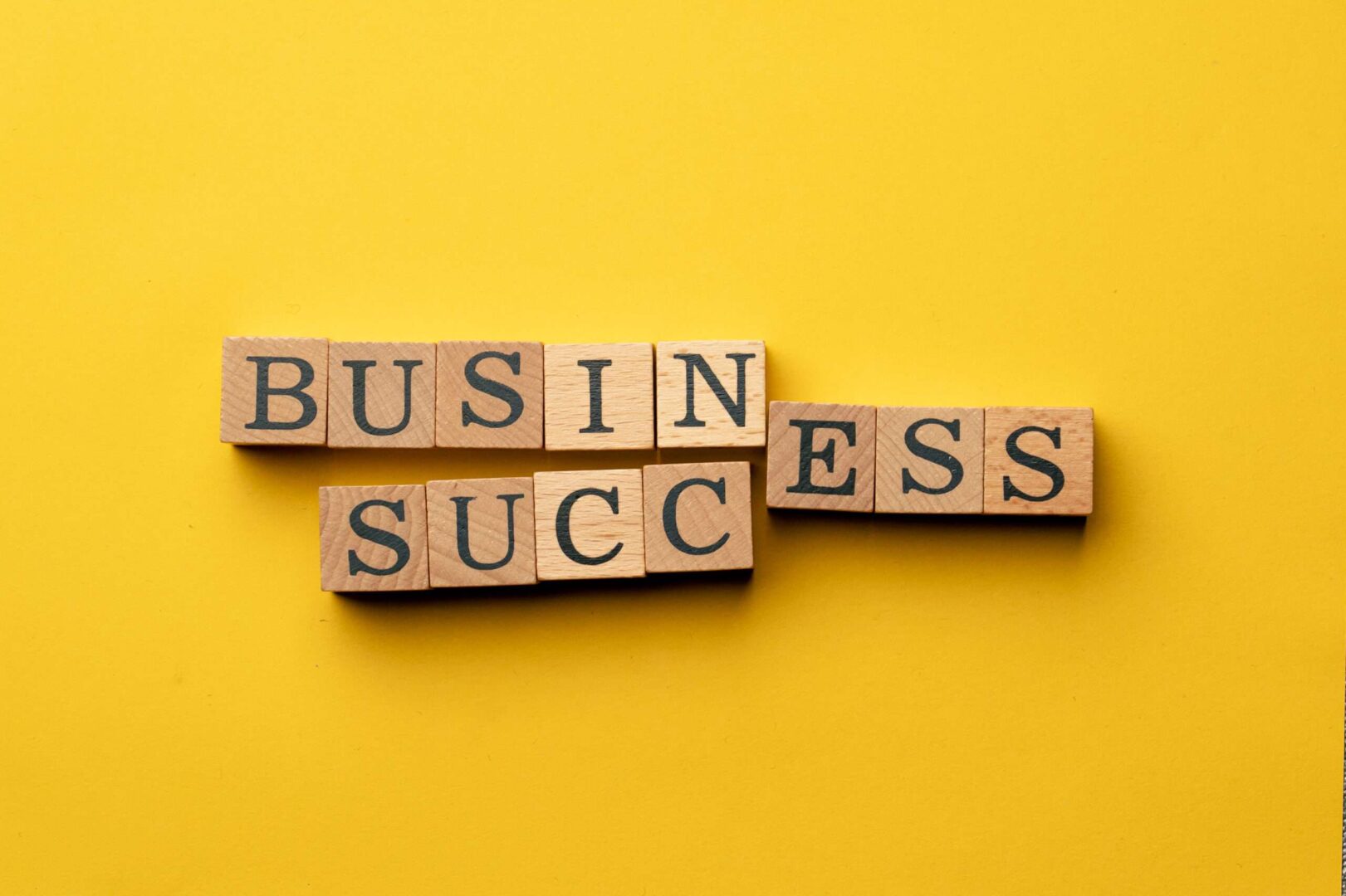 Wooden letter blocks spelling out "Business Success" on a yellow background, representing how Virtual General Counsel services help small businesses build a strong legal foundation for long-term growth.