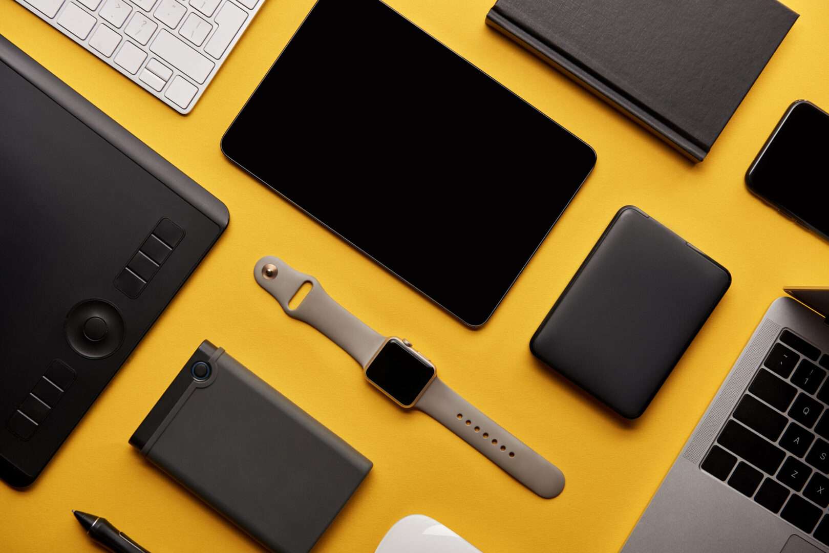 A flat lay of Apple tech devices including a tablet, smartwatch, laptop, keyboard, and accessories on a yellow background, representing the Apple executive overhaul and succession planning lessons every small business owner in Los Angeles should apply.