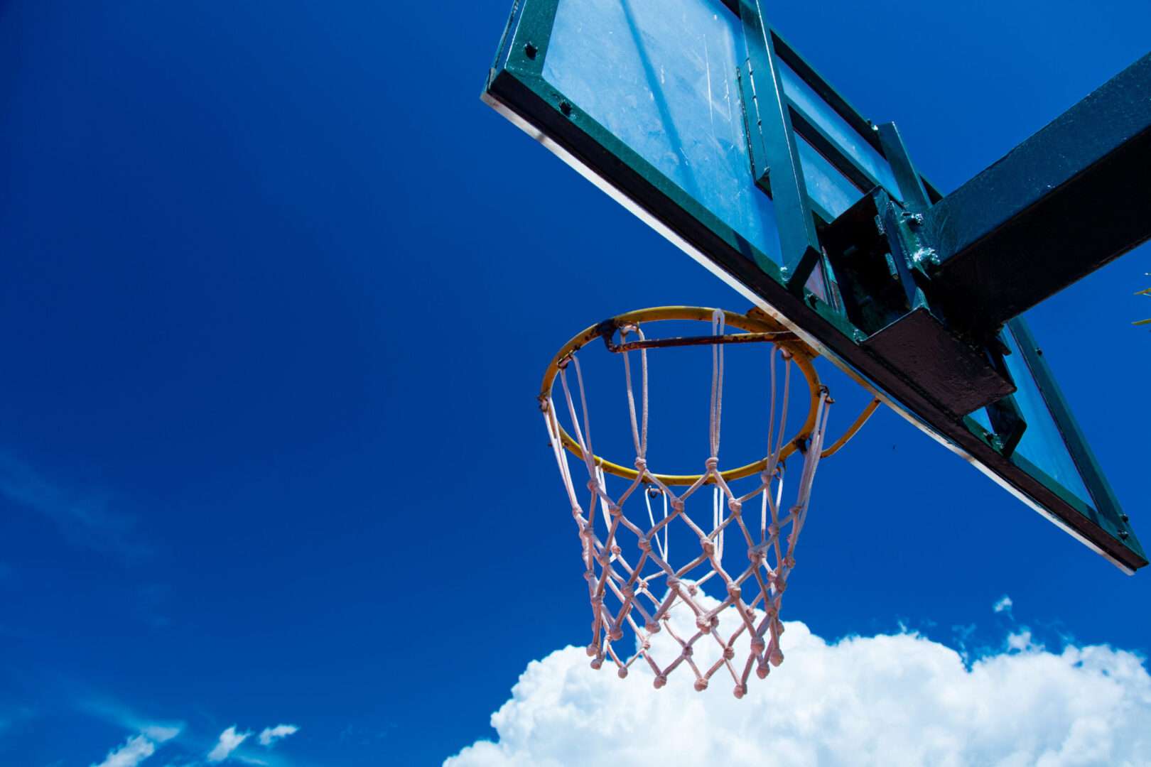 A basketball hoop with a glass backboard photographed from below against a bright blue sky with white clouds, symbolizing the championship persistence and brand-building lessons the Knicks offer small business owners.