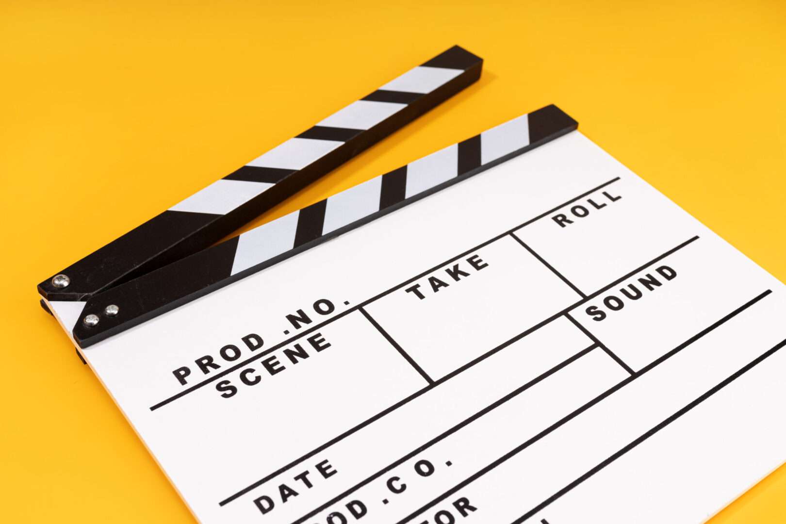 A digital film clapperboard with color calibration strips and labeled fields for scene, take, and director sits on a bright yellow surface beside audio gear, representing the legal and business lessons behind Spielberg's "Disclosure Day."