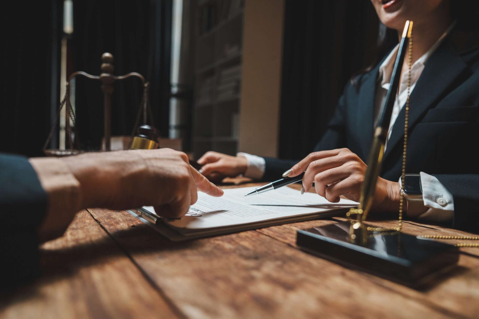 Two professionals review a legal agreement across a desk in an elegant office, with a set of justice scales and a gavel nearby, representing the regular legal checkups that keep a California LLC in good standing.
