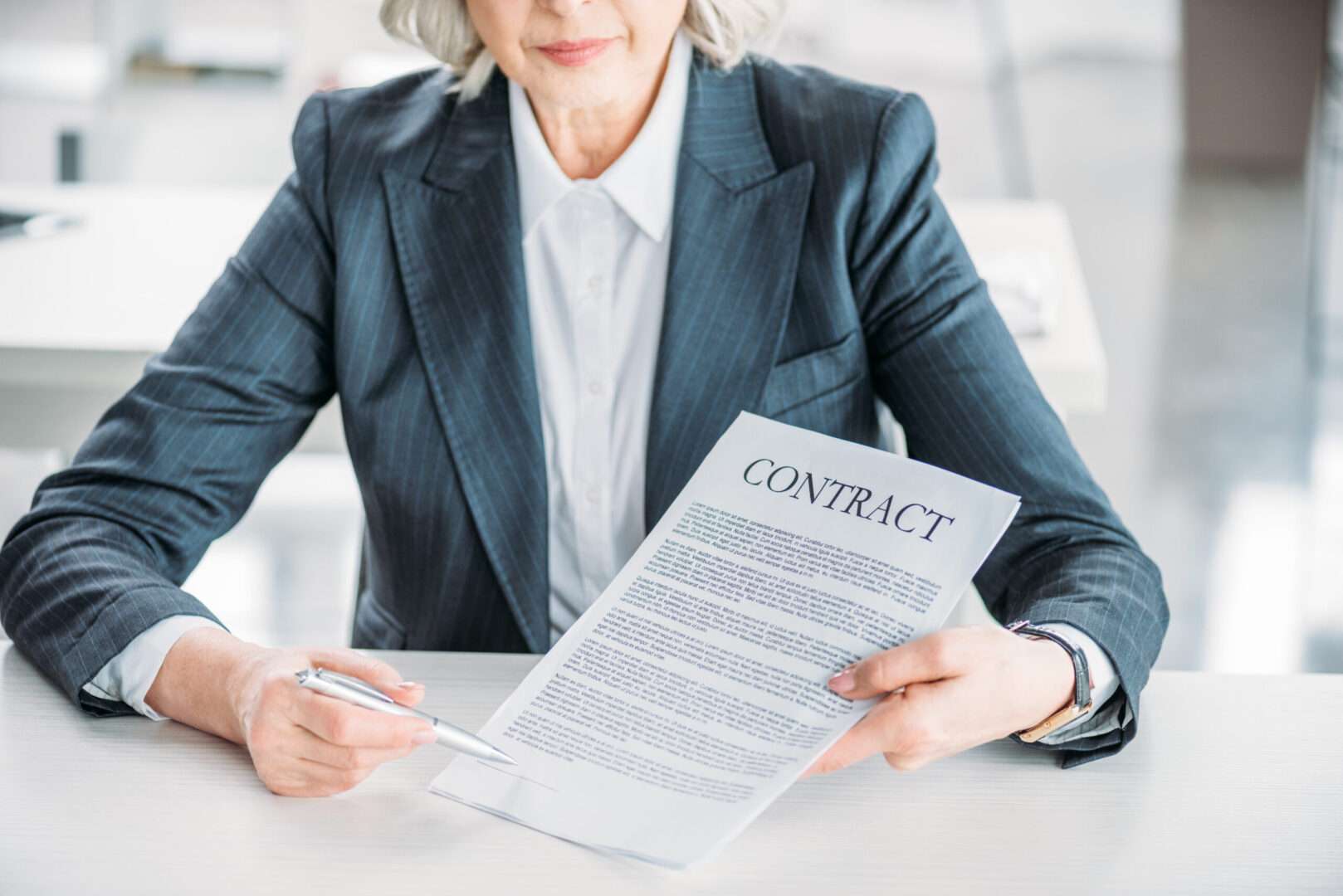 A businesswoman in a pinstripe suit holding a contract document and pointing to the signature line with a pen, representing the professional contract review services that protect online businesses in Los Angeles before they sign.