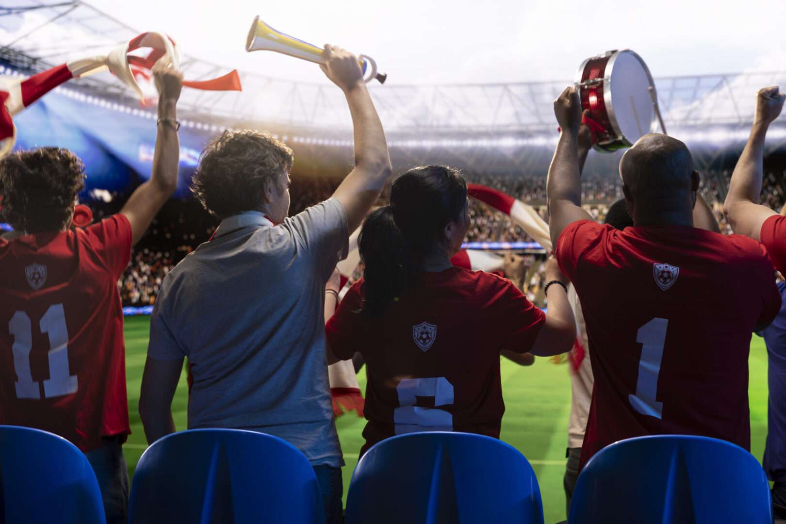 Soccer fans in red team jerseys cheer from the stands of a packed stadium, waving scarves, blowing a horn, and beating a drum, representing the World Cup crowds LA small businesses can legally capitalize on.