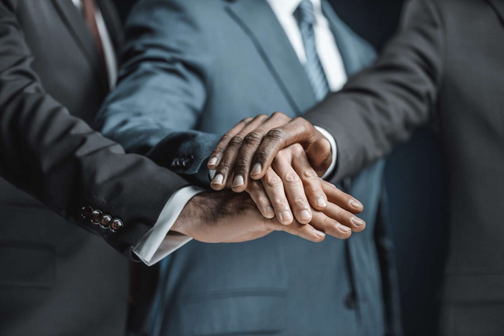 Three business professionals in suits stacking their hands together in a gesture of unity and partnership, representing the founder, investor, and legal team alignment needed to structure an entity correctly for QSBS before a fundraising round.