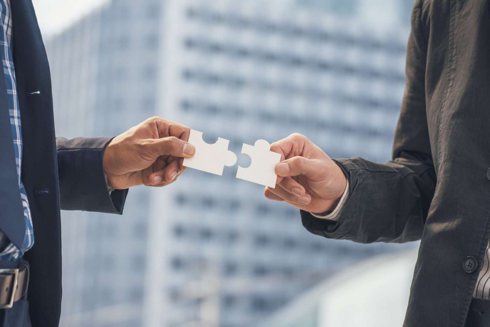 Two business professionals each hold a white puzzle piece and bring them together against a blurred city skyline, representing the careful structuring behind a corporate spin-off and business separation.