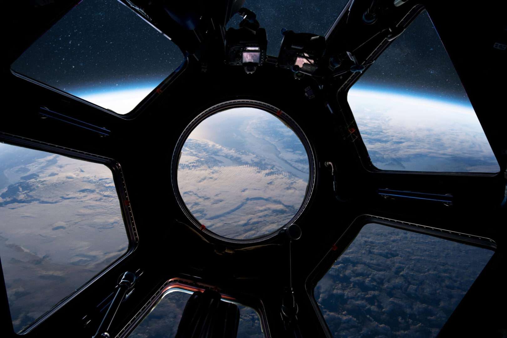 A view of Earth from space seen through the windows of a spacecraft cupola, with cameras mounted near the glass, evoking SpaceX's record IPO and the lessons it offers business owners about going public.
