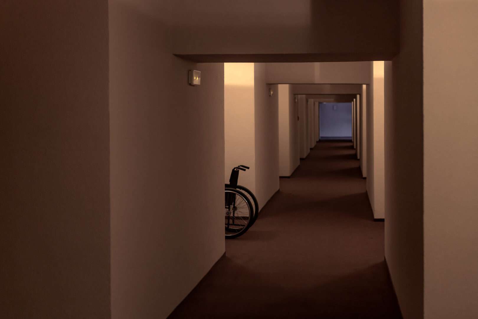 An empty wheelchair sits in a dim, eerie hallway with receding doorways, evoking the unsettling liminal spaces of the "Backrooms" horror phenomenon and the IP lessons it offers creators.
