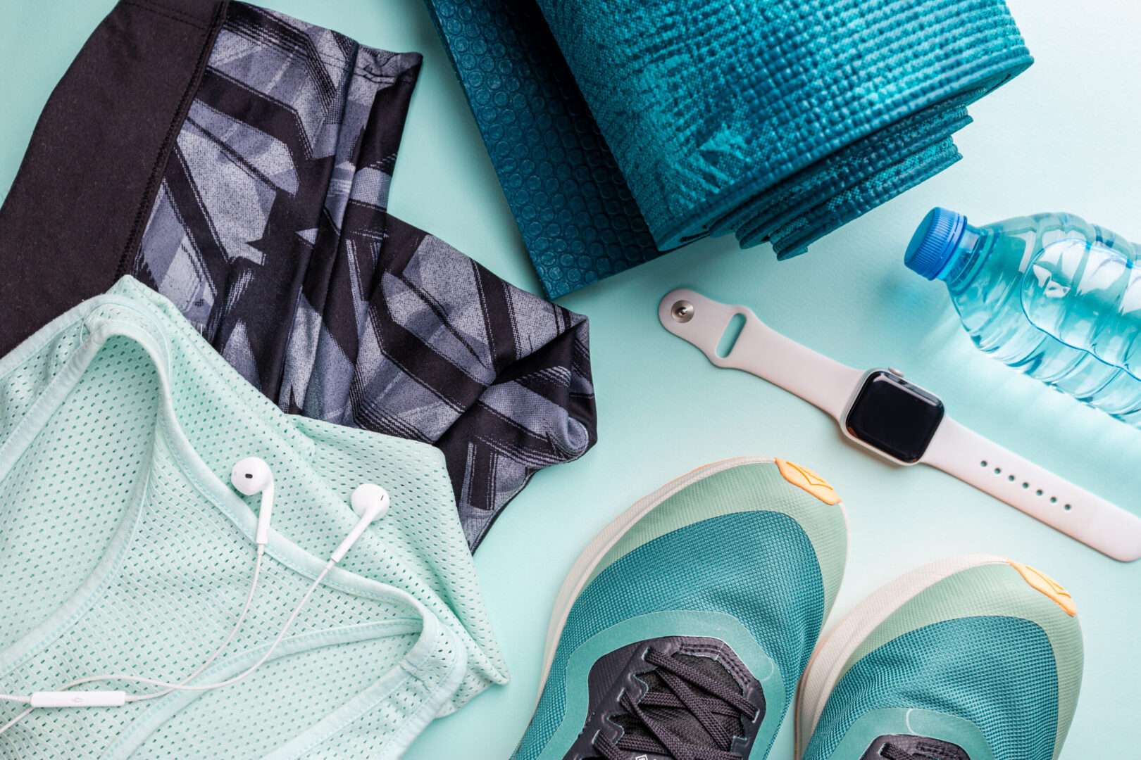 A flat lay of athletic apparel and fitness gear including leggings, a mesh tank top, running shoes, a yoga mat, a smartwatch, earbuds, and a water bottle on a light blue background, representing the activewear branding lessons from the Lululemon story for small businesses.