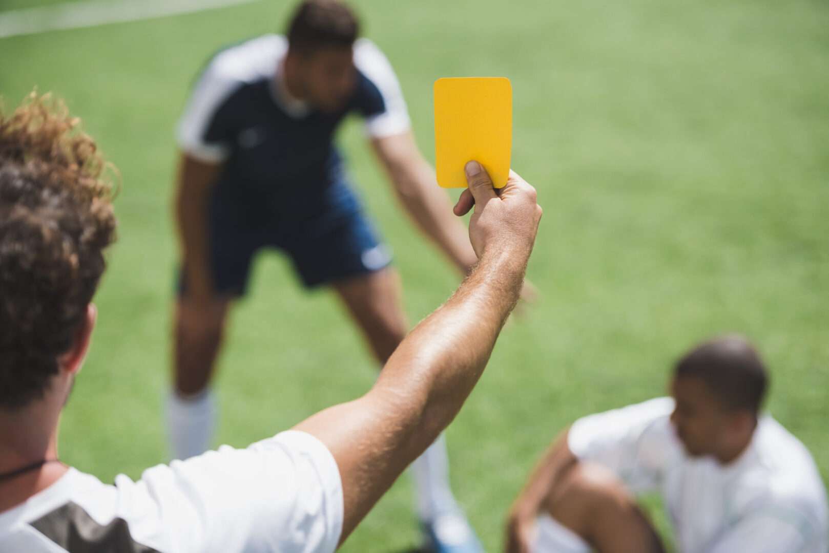 A soccer referee holds up a yellow card toward a player on a sunny field, representing the rule enforcement and dispute controversies from the 2026 World Cup and the business lessons they offer.