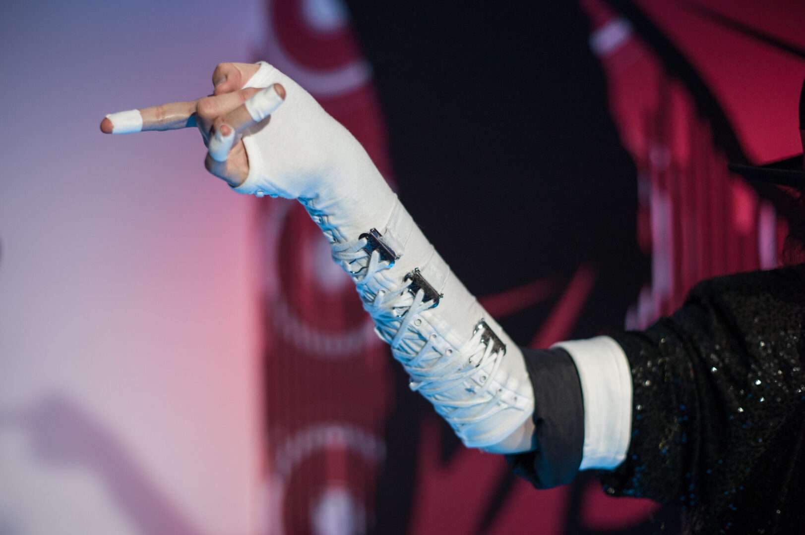 A performer's arm in a white laced glove and sleeve points outward against a stage backdrop, evoking Michael Jackson's iconic stage style and the estate licensing behind his biopic.