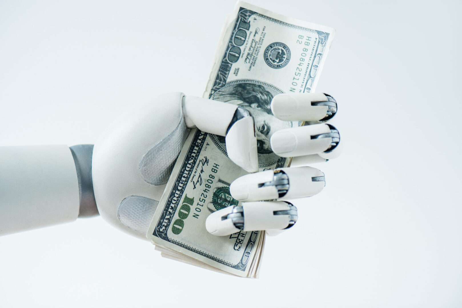 A close-up of a white robotic hand gripping a stack of one hundred dollar bills against a light background, representing how AI-driven costs are squeezing small business budgets and why contract clauses matter.