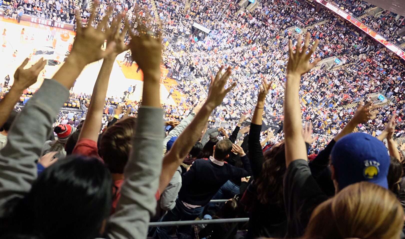 A crowd of fans with arms raised cheers during a packed indoor basketball arena, representing the fan loyalty and star power at stake when a franchise player leaves in NBA free agency.