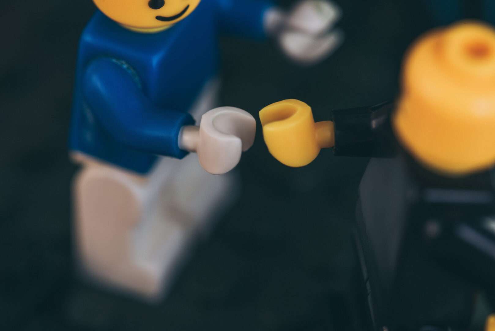 A close-up of two LEGO minifigures reaching out to touch hands against a dark background, representing the trust, agreements, and disputes at the heart of the Bricks and Minifigs consignment saga.