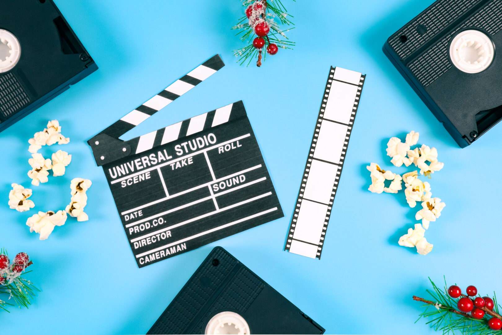 A movie clapperboard, a strip of film, popcorn, and vintage video tapes arranged on a blue background, representing the film industry and the intellectual property licensing behind blockbuster movies.