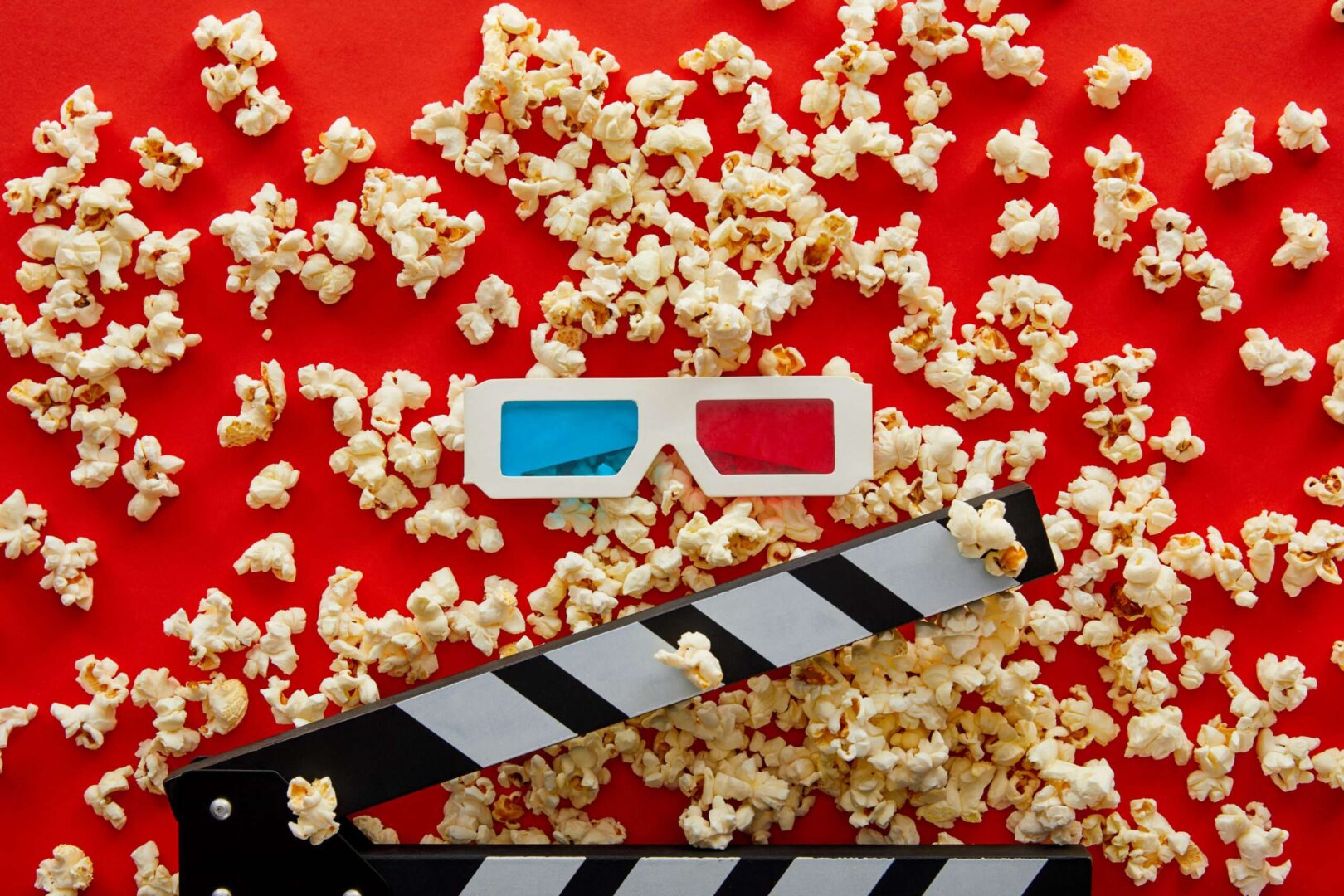 A movie clapperboard and 3D glasses rest on a red background scattered with popcorn, representing blockbuster box office economics and the franchise IP behind Spider-Man's record opening.