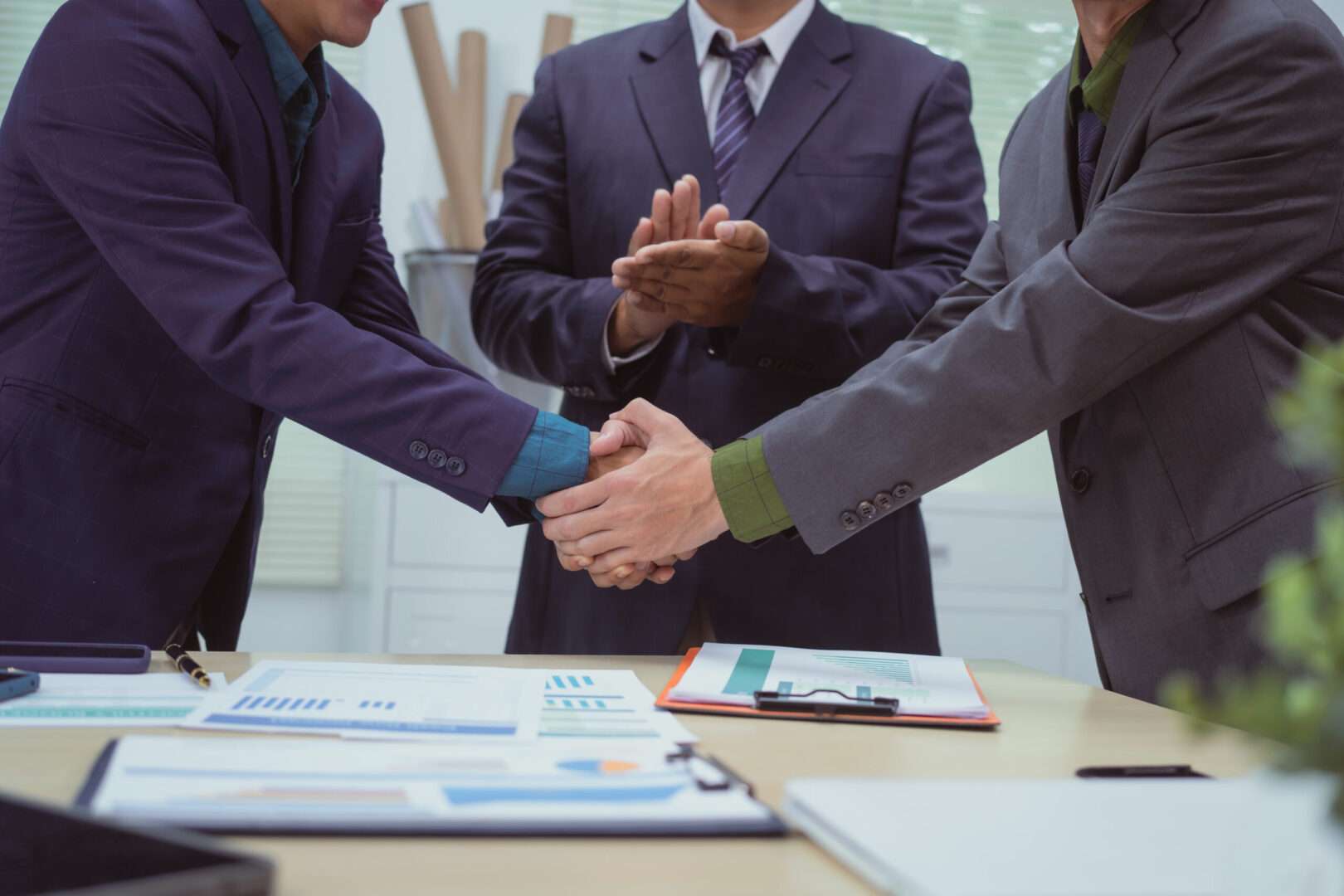 Business executives shaking hands over financial documents after closing a merger subject to California regulatory review