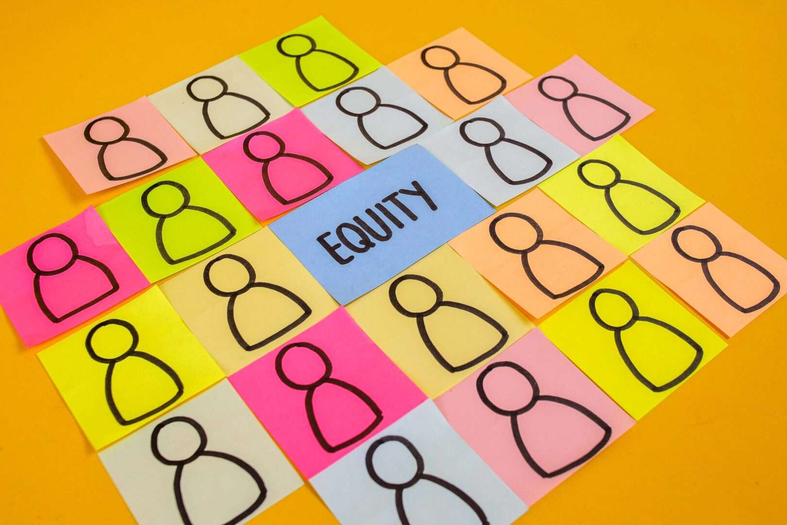 Brightly colored sticky notes with hand-drawn person icons surrounding a central blue note that reads "EQUITY" on a yellow surface.