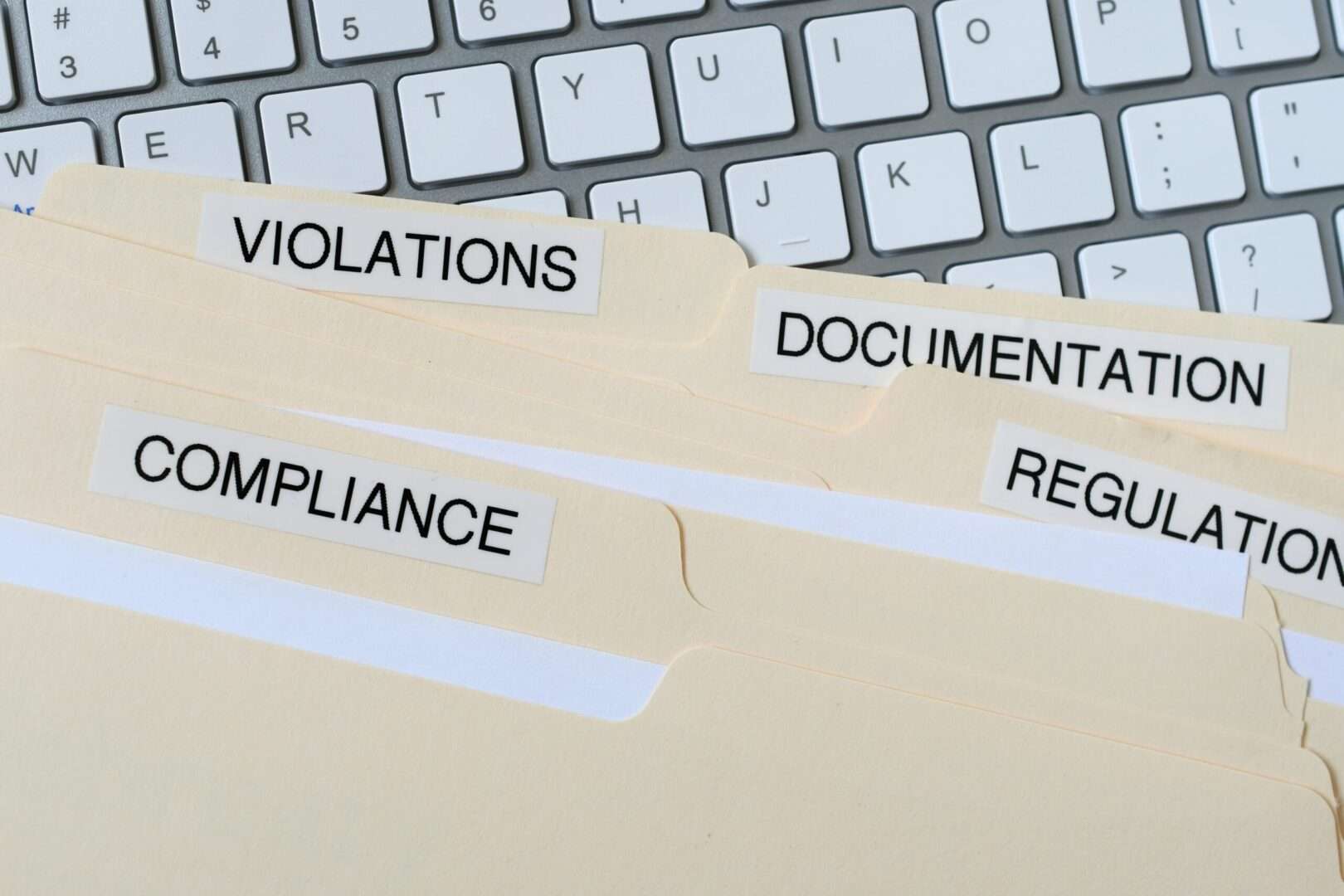 File folders labeled Compliance, Regulation, Documentation, and Violations on a keyboard, representing California business law changes taking effect in 2027