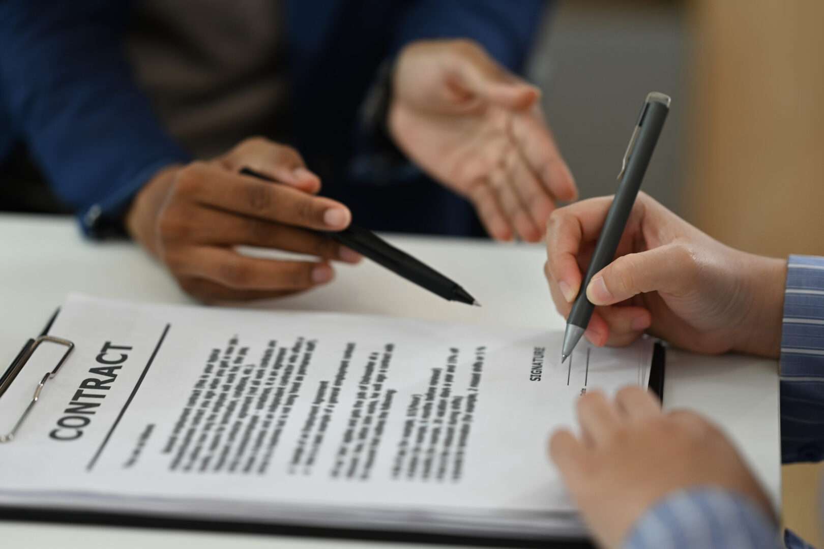Close-up of hands signing a business contract on a clipboard while another person points to the signature line, representing the DTC agreements that protect direct-to-consumer brands.