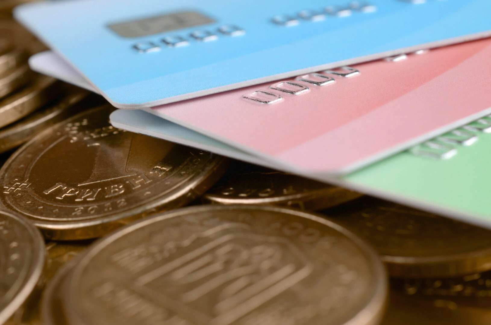 A close-up of three colored payment cards fanned out over a pile of gold coins, representing the separation between business and personal accounts that protects an LLC's liability shield.