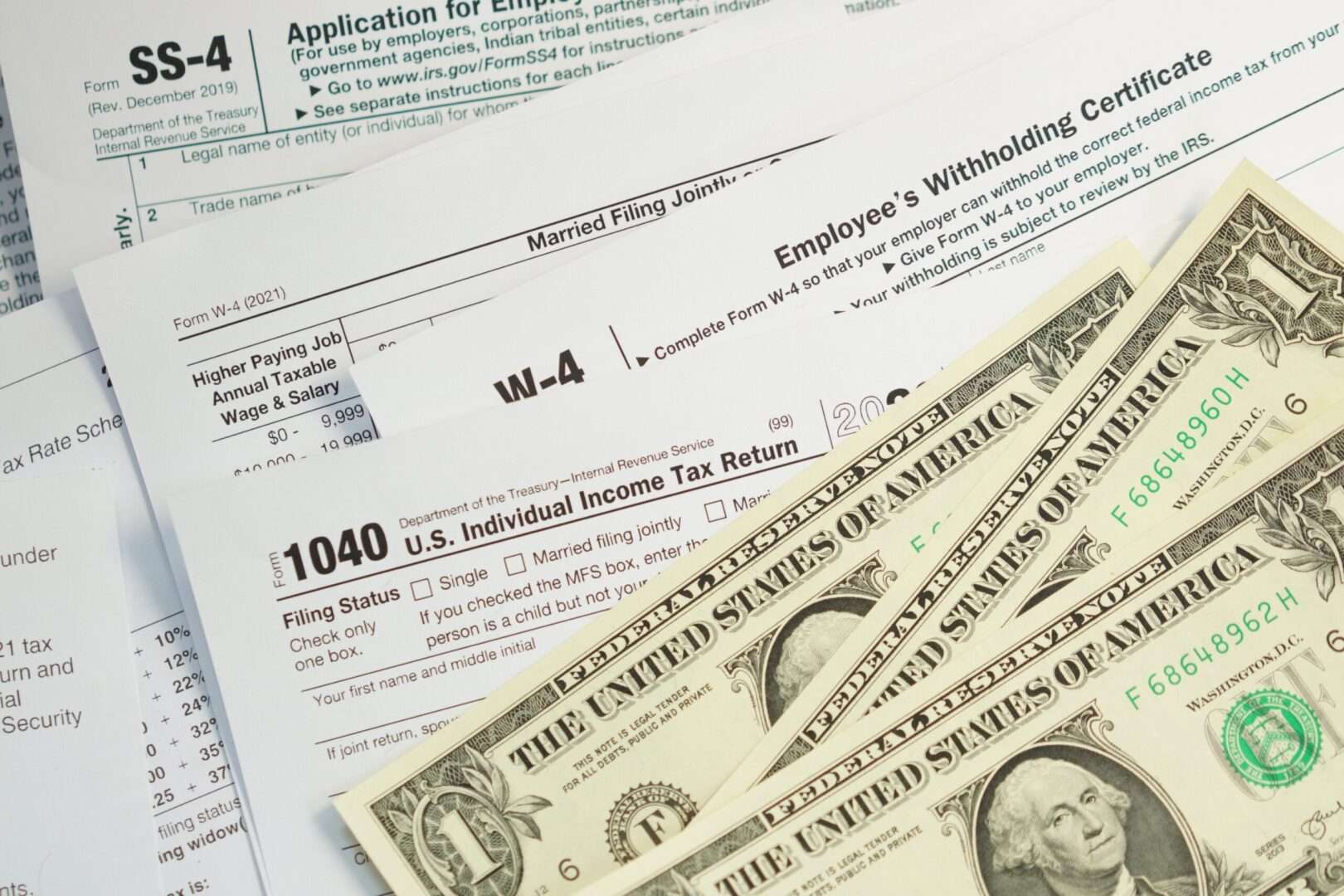 IRS tax forms SS-4, W-4, and 1040 with one dollar bills, illustrating independent contractor vs employee tax obligations in California