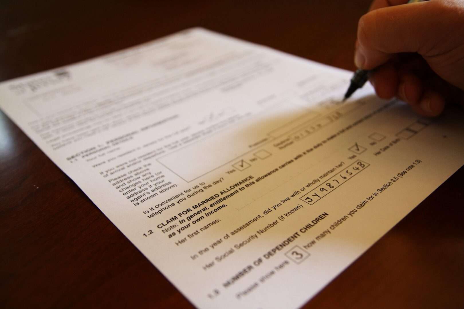 Close-up of a hand completing a printed form with a pen at a wooden desk