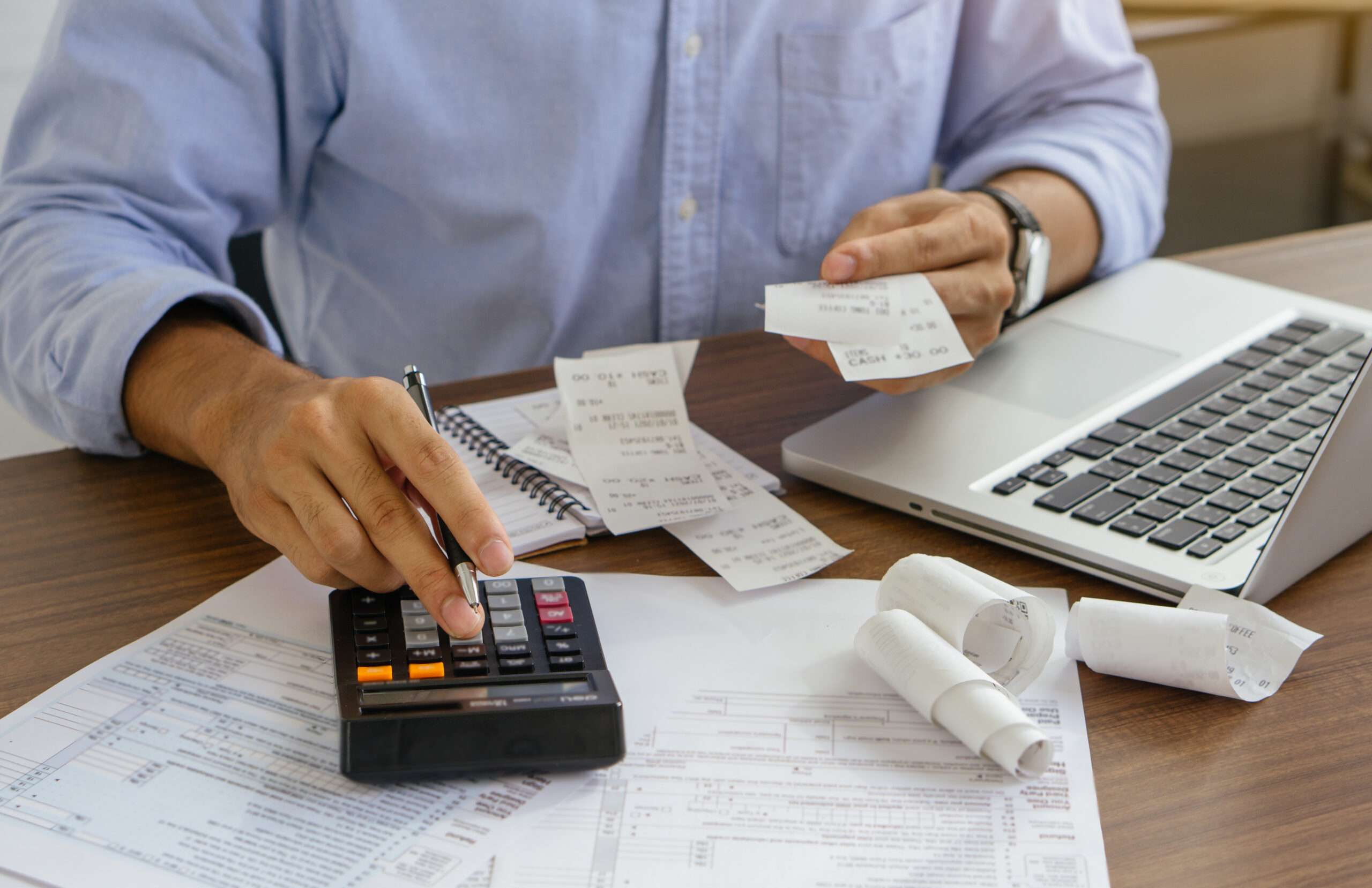 Business owner sorting receipts with a calculator, laptop, and tax form while reconciling accounts across multiple entities