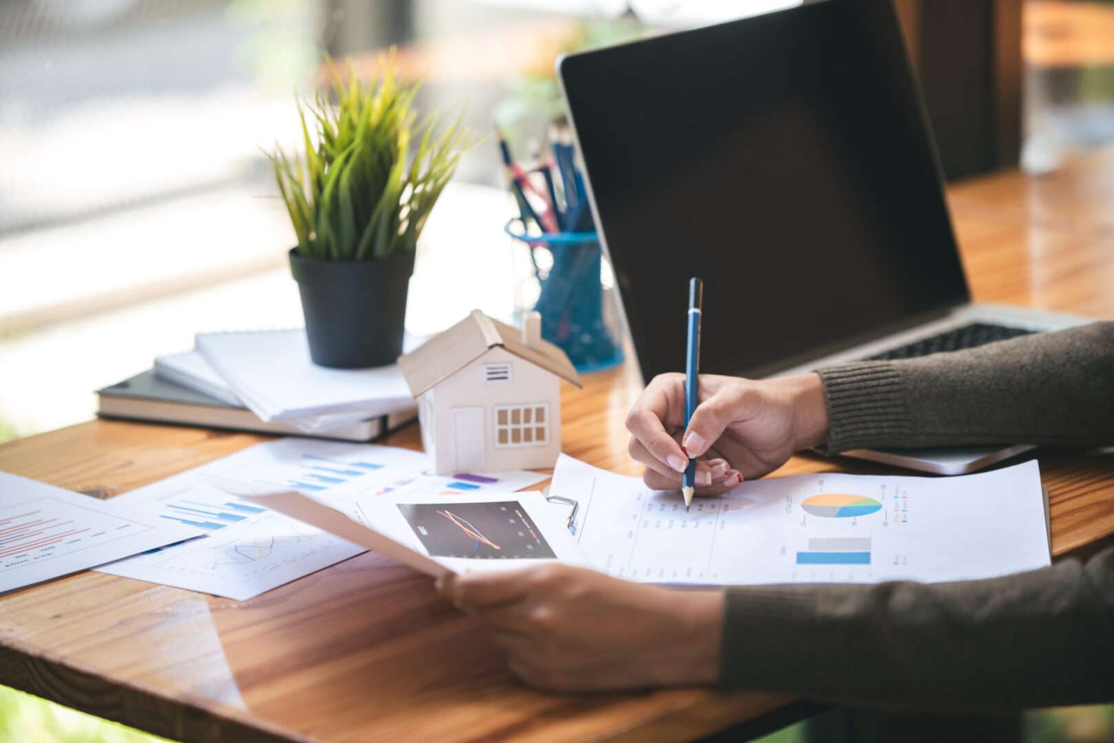 Real estate investor reviewing charts and financial reports at a desk with a laptop and a small model house