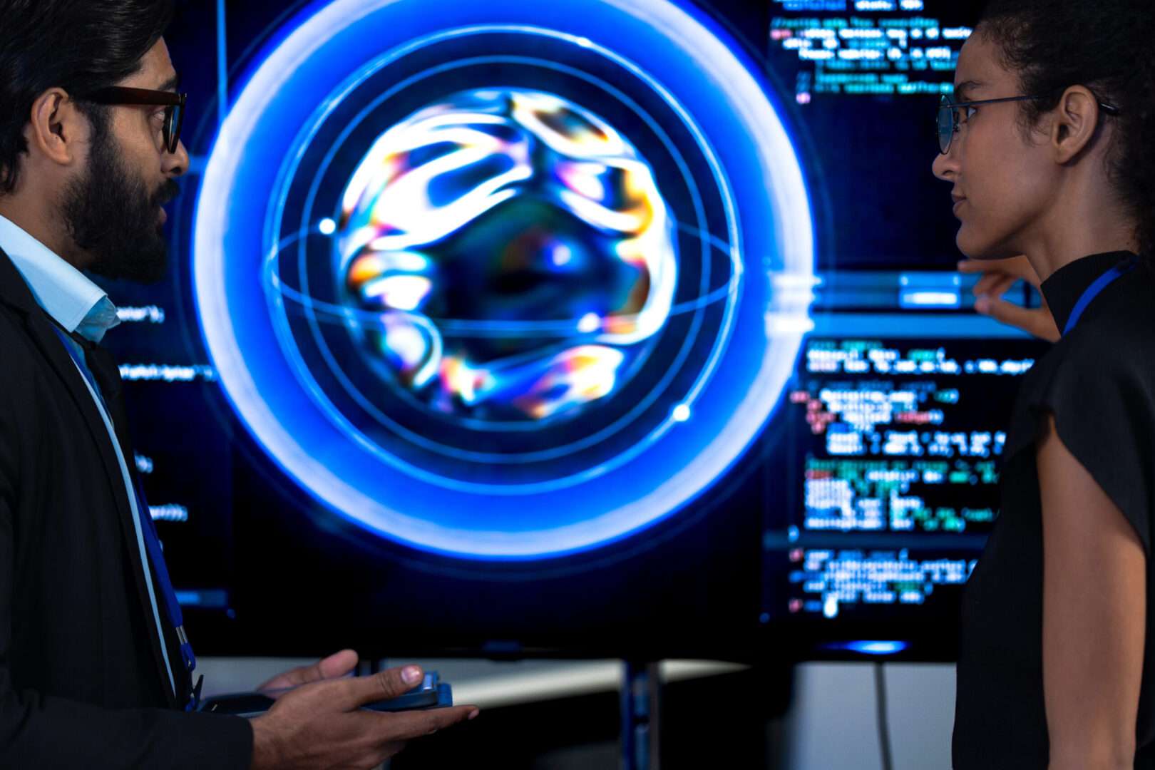 Two technology professionals discussing an AI system displayed on screens showing code and a generative model visualization