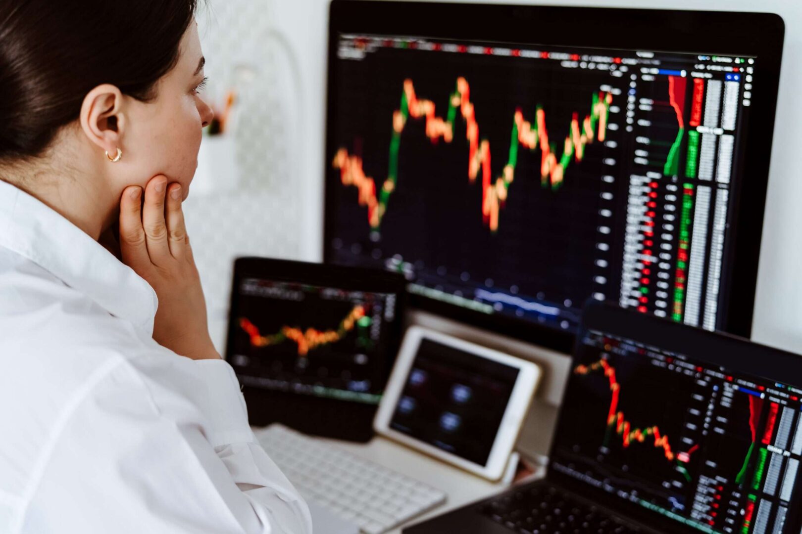 Woman studying stock price charts across several monitors and a tablet, representing how share value is assessed before granting stock options