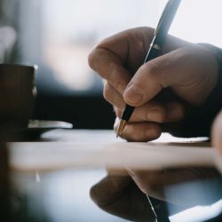 A close-up of a person's hand signing an important document with a classic pen, with a steaming coffee cup nearby, signifying a serious business negotiation or agreement.